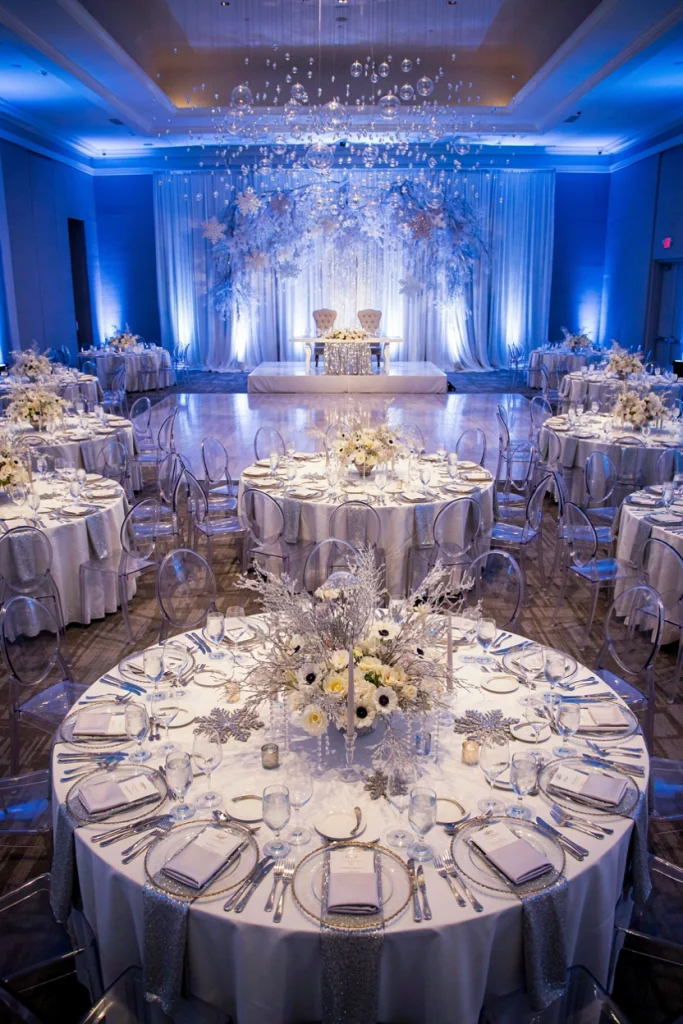 Medium sized ballroom wedding reception with sheer draped arch and silver charger place settings