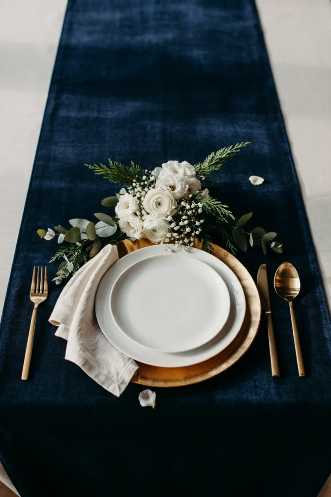 Full place setting with navy velvet linen, gold charger plate, and brass flatware